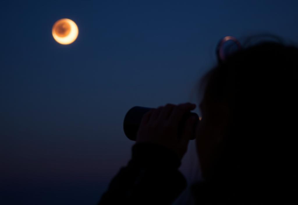 A person viewing a lunar eclipse through binoculars